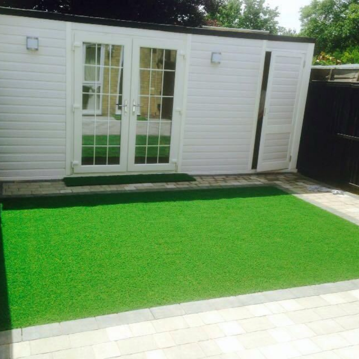 White garden room with French doors overlooking artificial lawn and paved patio